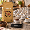 1 kg Lavazza Kaffeebohnen neben mehreren frisch zubereiteten Espressotassen